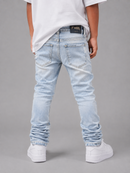 A child shown from the back wearing light-wash blue skinny jeans with gathered cuffs, a white t-shirt, and white sneakers against a solid gray studio background.