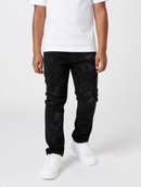 A person wearing black distressed skinny jeans with a subtle tonal pattern, paired with a white t-shirt and white sneakers, shown from the waist down on a light gray studio background.