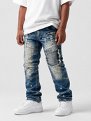 A child wearing distressed blue denim jeans with ripped details, a white t-shirt, and white sneakers, standing against a light gray studio background.