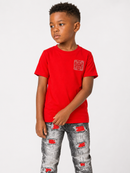 A young boy wearing a bright red short-sleeve t-shirt with a small red graphic on the left chest, paired with distressed gray jeans featuring red ripped details, photographed against a light gray studio background.