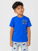 A young boy wearing a bright blue short-sleeve t-shirt with a textured geometric chest graphic and light-wash distressed jeans, standing against a light gray studio background.