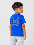 A young boy wearing a bright blue Saint Laurent t-shirt with a large blue logo graphic on the back, paired with light-wash jeans, photographed against a light gray studio background.