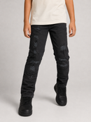 A person wearing black distressed skinny jeans with ripped details, paired with a cream t-shirt and black sneakers, shown from the waist down on a light gray studio background.