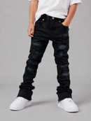 A child wearing black distressed denim jeans with faded blue wash details, styled with a white t-shirt and white sneakers against a solid gray studio background.