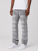 A person wearing light gray distressed jeans with horizontal frayed panel details and flap pockets, paired with a white t-shirt and white sneakers, against a light gray studio background.