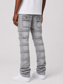 Light gray distressed denim jeans with unique patchwork paneling and frayed edges, shown on a model from the back wearing a white t-shirt and white sneakers.