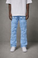 A person wearing light blue heavily distressed denim jeans with raw frayed edges, paired with a white t-shirt and white sneakers, standing against a gray studio background.