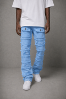 A person wearing light blue heavily distressed and frayed denim jeans, a white t-shirt, and white sneakers, standing against a gray studio background.