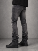 A person shown from the waist down wearing dark gray distressed skinny jeans and black shoes, standing against a textured gray studio background.