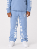 A child wearing a light blue sweatshirt and matching sweatpants with white graphic text and a broken-heart design, paired with white sneakers, photographed against a light gray studio background.