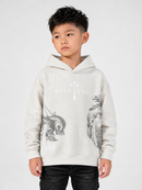 A young boy wearing a light gray hooded sweatshirt with a black and white graphic print featuring a cross, the word 'HOLY', and religious imagery, paired with black jeans, against a plain light gray background.