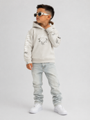 A young boy modeling a light beige hoodie with graphic prints, light-wash jeans, and white sneakers against a plain light gray background.