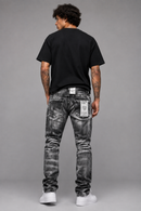 A man viewed from behind wearing a black t-shirt, black acid-wash slim-fit jeans with white sneakers, standing against a solid gray studio background. By Fresh N Fitted