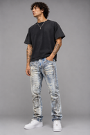 A man modeling a black crewneck t-shirt and light blue acid-wash distressed jeans with white sneakers, standing against a solid gray studio background. By Fresh N Fitted