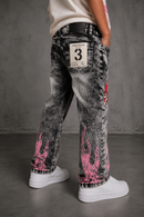 A person shown from the back wearing washed black denim jeans with bright pink flame graphics near the lower legs and a white patch on the back pocket, paired with white sneakers against a gray studio backdrop. by Fresh N Fitted