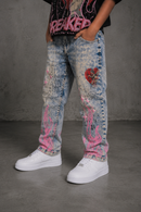 A person wearing light tint acid-wash distressed jeans with pink flame and red heart graphics, paired with white sneakers and a black graphic t-shirt, standing against a gray concrete wall. By Fresh N Fitted.