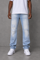 A person wearing light-wash distressed denim jeans with a white t-shirt and white sneakers, standing against a gray concrete wall. By Fresh N Fitted.