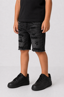 A child wearing distressed black denim shorts with a raw hem, paired with a black t-shirt and black sneakers, shown from the waist down against a light gray studio background.