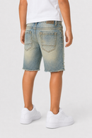 A child model shown from the back wearing light-wash blue denim shorts with a raw frayed hem, a white t-shirt, and white sneakers against a light gray studio background.