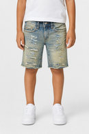A child wearing light-wash distressed denim shorts with frayed hems, paired with a white t-shirt and white sneakers, shown from the waist down against a light gray studio background.