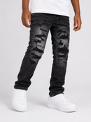 A person wearing black distressed denim jeans with a faded camouflage pattern on the thighs, styled with a white t-shirt and white sneakers, photographed against a light gray studio background.