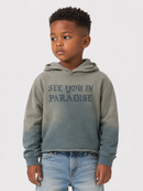 A young boy wearing a gray and blue gradient hoodie with 'SEE YOU IN PARADISE' printed on the front, paired with light blue jeans, against a light gray background.