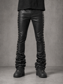 Black leather skinny jeans with silver-tone metal studs running down the outer sides, shown on a model from the waist down against a textured gray studio background.