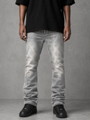 A person wearing light gray washed denim jeans with a subtle snakeskin pattern, styled with a black t-shirt and black sneakers against a textured gray studio background.