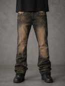A person wearing faded black jeans with gold glitter-like speckles, paired with a black shirt and black shoes, standing against a textured gray studio background.