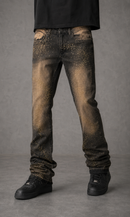 A person wearing distressed black denim jeans with a metallic gold glitter splatter pattern, styled with a black t-shirt and black sneakers against a gray studio background.
