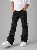 A person wearing black heavily distressed and frayed denim jeans, a white t-shirt, and white sneakers, standing against a solid gray studio background.