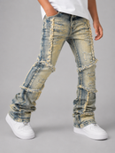 A person wearing light-wash distressed denim jeans with frayed patchwork seams and rips, paired with a white t-shirt and white sneakers, shown from the waist down on a gray studio background.