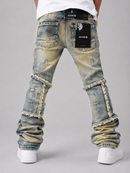 Rear view of a person wearing light-wash distressed denim jeans with frayed patchwork detailing and rolled cuffs, paired with a white t-shirt and white sneakers on a gray studio background.