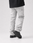 Light gray distressed denim jeans with frayed seam details and ripped knees, shown on a model from the waist down wearing black shoes against a light gray studio background.