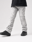 Light gray distressed denim jeans with frayed ripped details and cuffed hems, shown on a model wearing black sneakers against a light gray studio background.