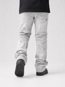 A person shown from the back wearing light gray distressed jeans with frayed cut details and black shoes, against a plain light gray studio background.