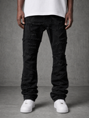 A person wearing black heavily distressed ripped jeans with frayed details, paired with a white t-shirt and white sneakers, standing against a textured gray studio background.