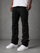 A person wearing distressed black jeans with heavily frayed, shredded detailing throughout, styled with a white t-shirt and white sneakers against a gray studio background.