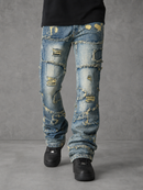 Distressed blue denim jeans with heavy rips, frayed edges, and yellowed faded patches, shown on a model wearing black shoes against a gray studio background.