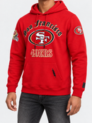 Model wearing a red Pro Standard San Francisco 49ers Old English hoodie, featuring team logo and fleece material.