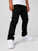 A person wearing black distressed skinny jeans with frayed cut details down the legs, styled with a white t-shirt and white platform sneakers against a light gray studio background.