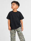 A young boy wearing a plain black short-sleeve t-shirt and distressed camouflage pants, standing against a light gray studio background.