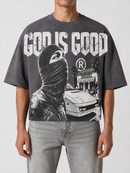 A man wearing a dark gray graphic t-shirt with a black and white print of a masked figure, a car, and the text 'GOD IS GOOD'.