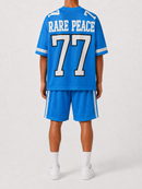 A model from the back wearing a bright blue short-sleeve jersey and matching shorts with white lettering that reads 'RARE PEACE' and the number '77', paired with white socks and sneakers on a light gray studio background.