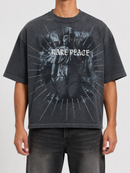 A person wearing an oversized faded black graphic T-shirt with a distressed religious figure print and the words 'HARE PEACE' across the chest, paired with dark jeans against a light gray studio background.