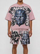 A model wearing a pink short-sleeve crop top and matching shorts set, both featuring a large black, white, and blue graffiti-style graphic print of a face.