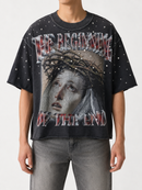 A person wearing an oversized black graphic T-shirt with a distressed print of Jesus' face, a crown of thorns, and the text 'THE BEGINNING OF THE END' in red and white, paired with gray jeans against a light gray studio background.