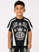 A young boy smiling and wearing a black and white athletic-style graphic t-shirt with 'LEGENDS CHAMPIONS' and lion graphics, paired with matching black shorts, against a light gray background.