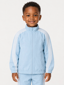 A young boy wearing a light blue zip-up track jacket with white stripes on the sleeves and matching light blue pants, photographed against a plain light background.