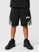 A child wearing black washed denim shorts with white flame motifs and the word 'REBEL' on the left leg, paired with black sneakers against a light gray studio background.